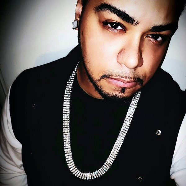 XiØN in a black vest over a white shirt, wearing a silver chain